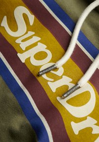 Sudadera con capucha de base verde, con el logotipo destacado de "SuperDry" en blanco y rayas horizontales multicolores en amarillo, granate y azul.