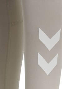 Beige legging met een gladde textuur, voorzien van witte chevronpatronen en contrasterende stiksels langs de naden.