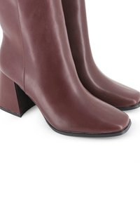 Botas de cuero marrón hasta la mitad de la pantorrilla, con puntas cuadradas y tacones de bloque, sobre un fondo blanco.