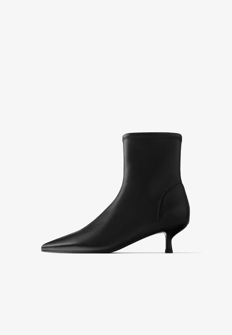 Bottine noire à bout pointu avec un petit talon kitten et une finition en cuir lisse, présentée en profil sur fond blanc.