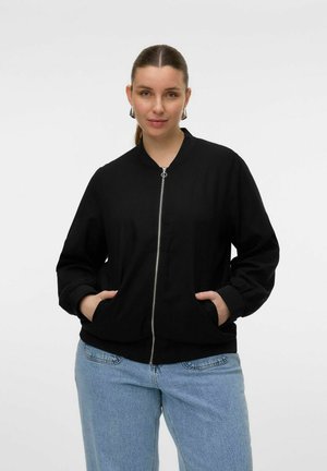 Veste bomber noire avec une fermeture éclair à l'avant, des poches latérales, des poignets côtelés et un col rond, associée à un jean bleu clair large.