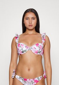 Conjunto de biquíni floral com uma base branca, apresentando padrões rosa e verde. A parte de cima tem alças com babados, e a parte de baixo inclui laços laterais com detalhes em metal.