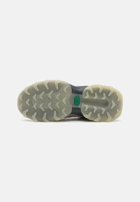 Sport shoe outsole with a textured, gray rubber material. Its pattern features triangular lugs for grip and a prominent green logo.