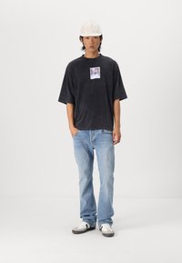 Sort oversized t-shirt med et grafisk tryk foran, lyseblå jeans og hvide sneakers med grå detaljer, komplementeret af en hvid kasket.