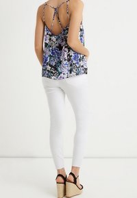 Blommig tanktop i svart, lila och blå med en strappy ryggdesign; kombinerad med vita tajta byxor och svarta kilklackar.