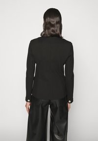 Blazer negro ajustado con mangas largas, que presenta un corte recto, un solo botón en el puño y una textura de tela suave.