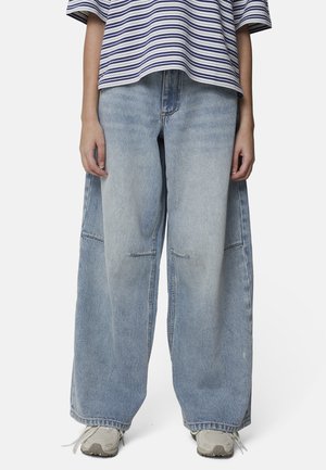 Personne portant un jean large bleu clair, des baskets blanches et un t-shirt à manches courtes rayé avec des lignes horizontales bleues et blanches.