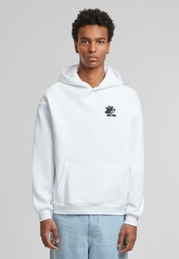 Sweat à capuche blanc avec une poche avant et un logo graphique noir sur la poitrine. Le tissu semble doux, avec une coupe décontractée et des manches longues standard.