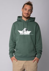 Un sweat à capuche vert en matériau doux, orné d'un graphisme de bateau en papier blanc et d'une poche kangourou. Des cordons de serrage réglables complètent le design.
