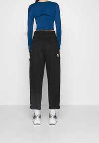 Dlouhý rukáv modrý cropped top v kombinaci s černými cargo kalhotami s kapsami a našitím na boku, doplněný bílými teniskami.