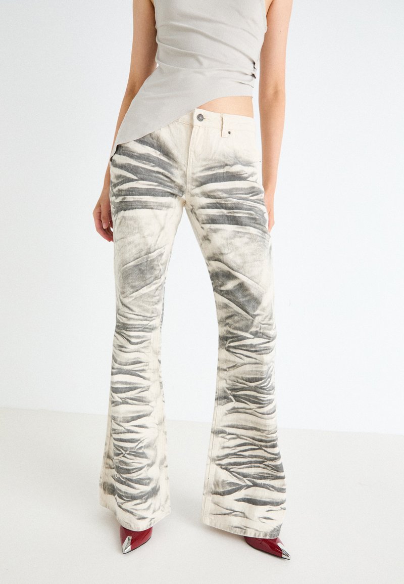 Flared jeans in cream with gray creased patterning, featuring a button front closure and five-pocket design. Smooth fabric texture.