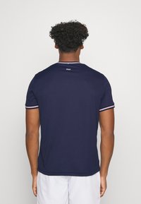 Laivastonsininen lyhythihainen paita, jossa valkoiset ja punaiset raidat kauluksessa ja hihoissa. Pehmeä kangas, normaali istuvuus, logo takana.