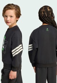 Čierna mikina so disneyovskou grafikou, okrúhlym výstrihom a širokými bielymi pruhmi na rukávoch. Tkanina má hladkú textúru a uvoľnený strih.