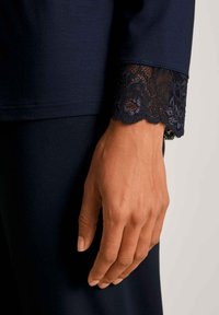 Navy lange mouw kledingstuk met een kantafwerking aan de manchette, dat ingewikkelde bloemmotieven toont. Gladde stofstructuur, close-up van een hand.