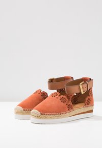 Espadrillas in suede arancione con motivo floreale a intagli, cinturino alla caviglia e suola avvolta in juta. Suola in gomma bianca per aderenza.