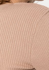 Ribbed knit sweater in a soft blush color, featuring a round neckline and a smooth texture with visible seams on the shoulder area.