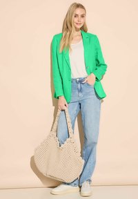 Grön blazer över vit topp, ljusblå jeans och en beige virkväskan. Sneakers med texturerade sulor. En enkel, avslappnad outfit.