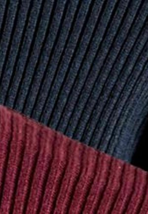 Gerippter Pullover mit Farbblock-Design, oben dunkelblau und unten tiefrot. Texturierte, gestrickte Materialien sichtbar.