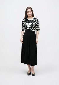 Black and white patterned top with three-quarter sleeves paired with a black pleated skirt, featuring a fitted waistband and smooth texture.