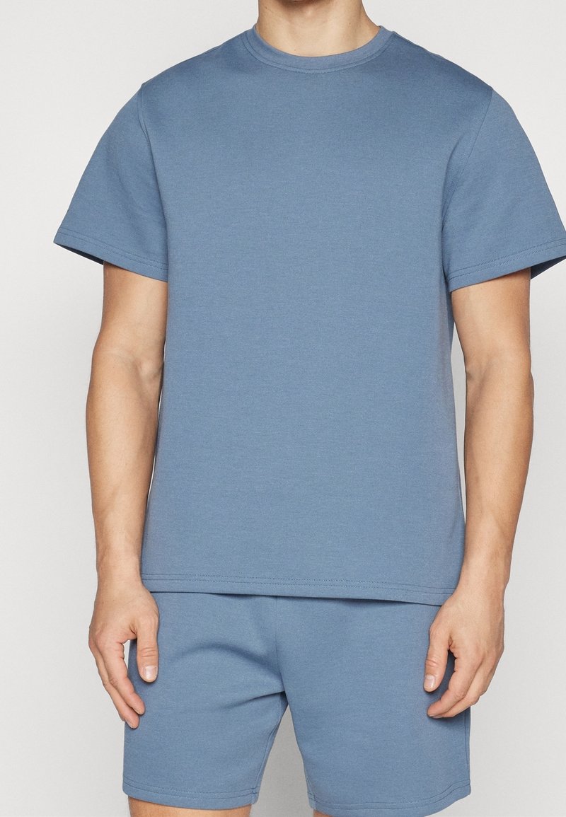 T-shirt en coton bleu clair avec col rond et manches courtes, accompagné de shorts assortis. Texture douce, design simple, sans motifs ni accents.