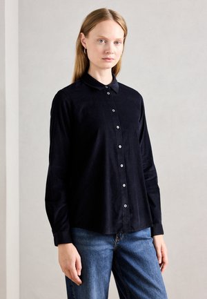 Black button-up shirt with a soft texture, a collar, and long sleeves, paired with blue jeans. Features silver buttons along the front.