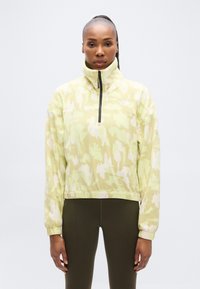 Φλις πουλόβερ σε ανοιχτό πράσινο με αφηρημένα λευκά σχέδια, φερμουάρ στον λαιμό, ψηλό γιακά και ελαστικά μανσέτες. Σχεδιασμένο για άνεση και ζεστασιά.