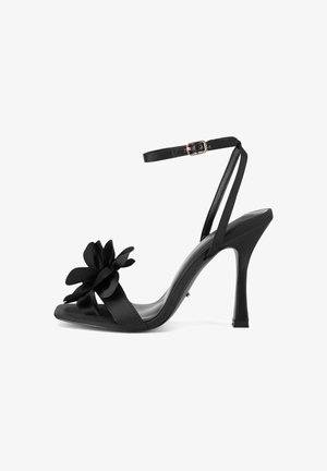 Juoda satino aukštakulnė basutė su atviru pirštu, ant dirželio puikuojasi gėlių akcentas, o šlaunies dirželis yra plonas ir su sagtimi.