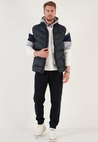 Vadderad grå och marin väst över en vit hoodie, kombinerad med marin joggingsbyxor och vita sneakers med en flerfärgad detalj.