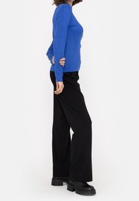 Blå ribbade långärmade toppar i kombination med svarta vida byxor och svarta klumpiga klackstövlar, sedd från sidan.