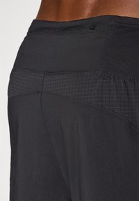 Schwarze Sportshorts verfügen über einen strukturierten Bund mit einem Rautenmuster. Der Stoff wirkt leicht und strapazierfähig und ist für aktive Nutzung konzipiert.
