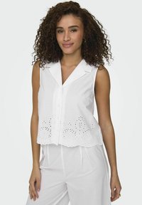 Blusa bianca senza maniche con colletto, caratterizzata da ricami ad occhio lungo l'orlo, realizzata in cotone leggero e con chiusura frontale a bottoni.