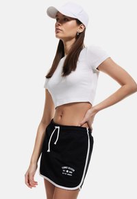 Witte pet, aansluitend wit crop-top en zwarte rok met trekkoord, afgewerkt met een witte rand en de tekst "TENNIS SEASON" op de voorkant. Gladde stof en sportieve stijl.