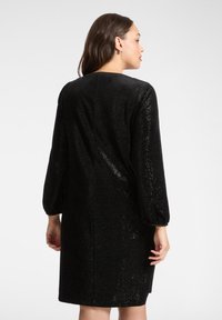 Vestito nero in paillettes con maniche lunghe a sbuffo, taglio dritto e scollo rotondo. Il tessuto ha una finitura lucida e strutturata.