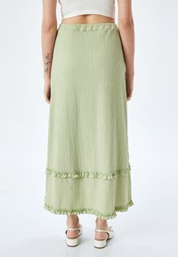 Hellgrüßer, gestufter Maxikleid aus zerknittertem Stoff mit gerüschten Säumen. Der Bund ist elastisch und sorgt für eine bequeme Passform.