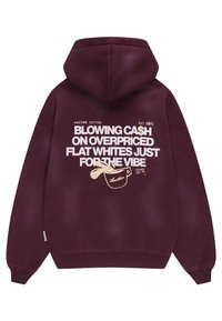 Sweat à capuche marron avec texte blanc indiquant ""Blowing cash on overpriced flat whites just for the vibe"" et illustration d'une tasse à café beige au dos.