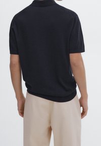 Musta lyhythihainen poolopaita, neulottu rakenne ja klassinen kaulus. Suunniteltu rentoon istuvuuteen ja hieman kaartuvaan helmaan.