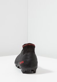 Black soccer cleat with red "Predator" text, ribbed ankle collar with red stitching, and molded studs on a white surface.