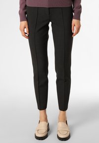 Pantaloni tailored grigio scuro con una vestibilità slim, dotati di pieghe frontali, abbinati a mocassini beige. Il materiale appare liscio con una leggera lucentezza.