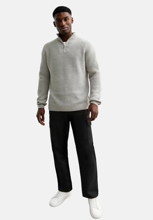 Light gray, ribbed knit sweater with a half-zip collar, paired with black cargo pants and white sneakers, creating a casual look.
