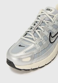 La sneaker Nike présente un dessus en maille argentée avec des accents noirs, des superpositions texturées et une semelle en caoutchouc. Les lacets sont gris clair et assurent un bon maintien.