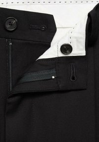 Zwarte broek met gedeeltelijk open rits, twee zwarte knopen en een binnenvoering van witte stof met zwarte stiksels.