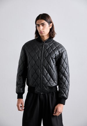 Veste bomber matelassée noire en matériau brillant, avec un col, des poignets et un ourlet côtelés, dotée d'une fermeture éclair à l'avant et de poches zippées sur les côtés.