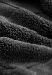 Närbild av mjuk, texturerad mörkgrå fleece med synliga slingor och veck som skapar en plyschyta.