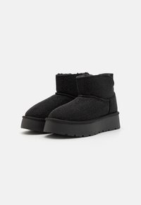 Botine negre până la glezne, cu un material texturat, având mici accente strălucitoare, o căptușeală interioară moale și o talpă platformă joasă, masivă.