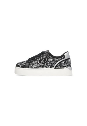 Niedriger schwarzer Sneaker mit silbernen Nieten, schwarzen Schnürsenkeln, weißer dicker Sohle und metallisch silbernem Fersenakzent, der ein rundes Logo an der Seite zeigt.