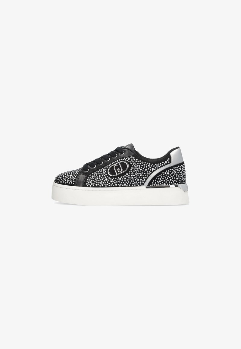 Baskets basses noires avec studs argentés, lacets noirs, semelle blanche épaisse et accent métallique argenté au talon, affichant un logo circulaire sur le côté.