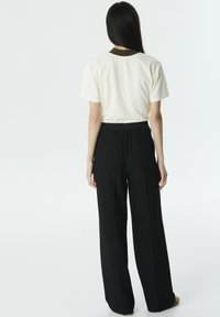 Top corto crema con maniche corte e colletto marrone, abbinato a pantaloni larghi neri a vita alta con elastico in vita e tasche posteriori.