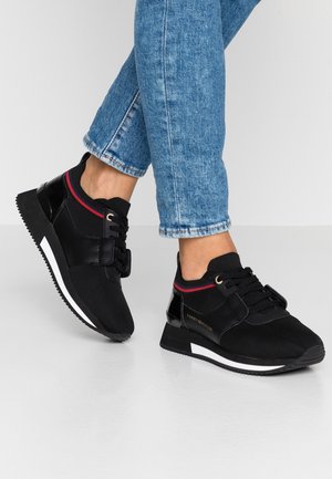 Czarne sneakersy na sznurówki z czerwonymi i białymi paskami, noszone z niebieskimi dżinsami, pokazujące widoki boczne i z góry na jednolitym tle.