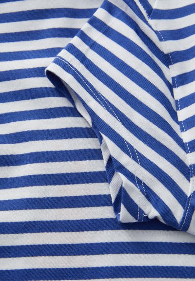 Tissu rayé horizontal bleu et blanc avec une manche repliée, montrant des coutures détaillées le long des bords.