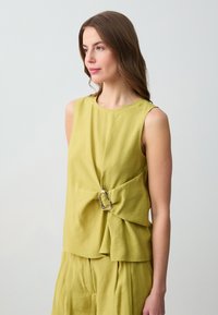 Top senza maniche verde lime con design attorcigliato, fibbia argentata e texture morbida. Abbinato a un fondo plissè coordinato.